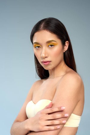 beauty and grace, asian model with bold makeup and bare shoulders posing on blue backdrop