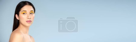 Téléchargez les photos : Portrait, femme asiatique avec maquillage audacieux et épaules nues regardant loin sur fond bleu, bannière - en image libre de droit