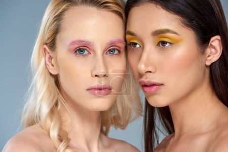 vielfältiges Schönheitskonzept, interrassische Frauen mit kühnem Augen-Make-up posieren auf blauem Hintergrund, feminin