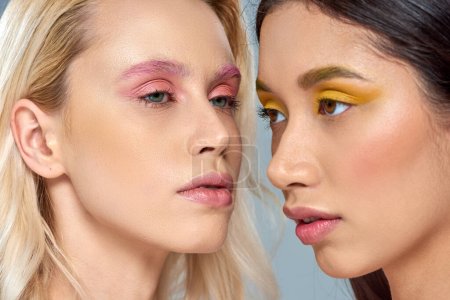 Vielfältiges Schönheitskonzept, multiethnische Frauen mit lebendigem Augen-Make-up posieren gemeinsam vor blauem Hintergrund