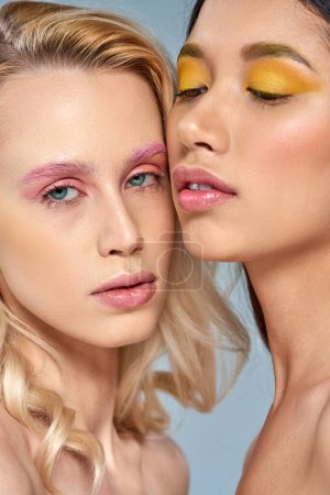 diverse beauty concept, interracial women with vibrant eye makeup posing together on blue backdrop