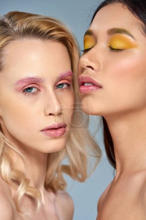 feminine beauty concept, interracial women with vibrant eye makeup posing together on blue backdrop