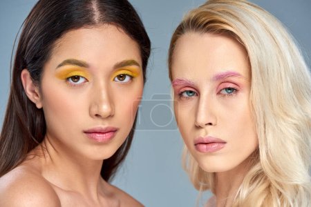 interracial models with bold eye makeup posing together on blue backdrop, beauty trend concept