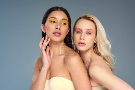 diverse young models with bold eye makeup posing together on blue backdrop, beauty trend concept