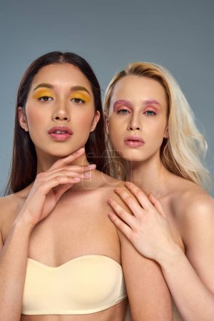 diverse models with vibrant eye makeup looking at camera on blue backdrop, beauty trend concept