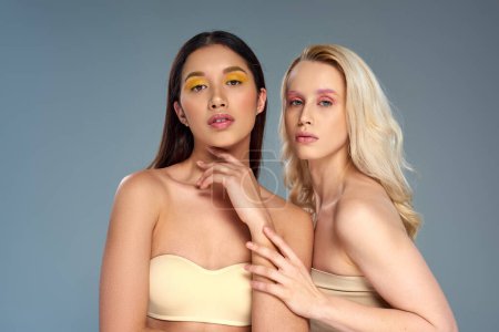 Models mit kühnem Augen-Make-up posieren in Unterwäsche vor blauem Hintergrund, vielfältiges Schönheitskonzept