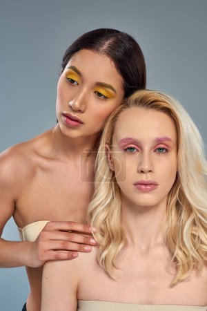 multiethnische Models mit kühnem Augen-Make-up posieren gemeinsam auf blauem Hintergrund, vielfältiges Schönheitskonzept
