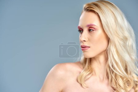 modelo sensual con maquillaje de ojos rosados y cabello rubio mirando hacia otro lado en el fondo gris, belleza femenina