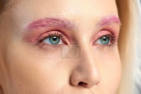 photo détaillée de jeune femme aux yeux bleus et fards à paupières roses regardant loin, gros plan