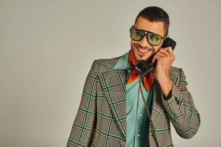 happy man in plaid blazer and sunglasses talking on vintage telephone on grey, retro fashion