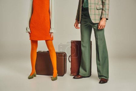 Ausgeschnittene Ansicht von Retro-Reisenden in orangefarbenem Kleid und kariertem Blazer in der Nähe von Vintage-Koffern auf grau