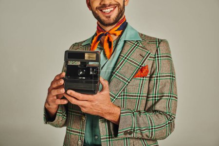 vue recadrée d'un homme souriant vêtu d'une veste à carreaux tenant une caméra vintage sur un style de vie gris et rétro