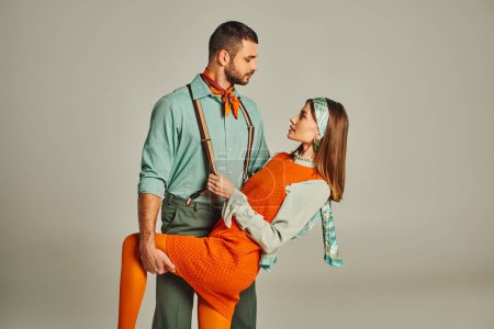Téléchargez les photos : Homme à la mode dans les bretelles flirter avec la femme en robe orange sur gris, mode d'inspiration rétro - en image libre de droit