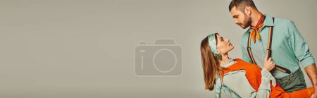 Téléchargez les photos : Vue latérale de l'homme confiant dans les bretelles flirter avec la femme dans des vêtements rétro lumineux sur gris, bannière - en image libre de droit