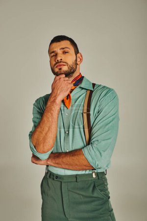 Nachdenklicher Mann in Hosenträgern und hellem Halstuch, der auf graue Vintage-Mode in die Kamera blickt
