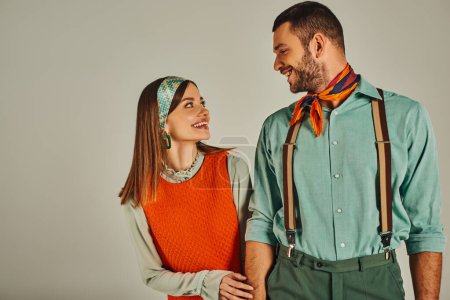 joven y alegre pareja en elegante ropa antigua mirándose el uno al otro en el fondo gris