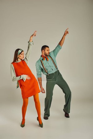 Stylisches Paar in Vintage-Kleidung tanzt mit erhobenen Händen auf grau, Retro-Vibes und Aufregung