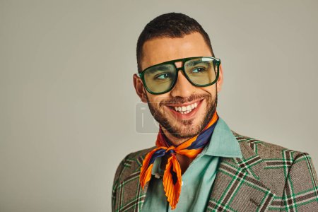glücklicher Mann in karierter Jacke und hellem Halstuch mit Sonnenbrille, der vom grauen Vintage-Stil absieht