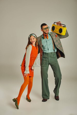 glückliches altmodisches Paar mit gelber Boombox, das auf Grau, Unterhaltung und Retro-Lifestyle tanzt