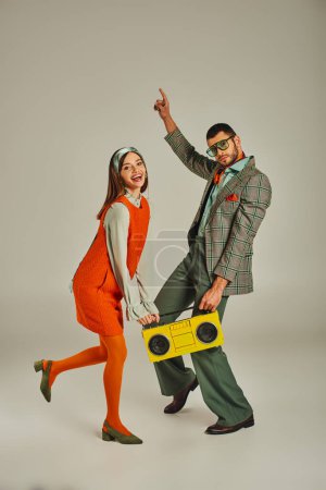 alegre pareja a la antigua con boombox amarillo bailando en gris, felicidad y estilo de vida retro