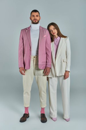 longitud completa de la pareja joven en ropa formal con estilo mirando a la cámara en gris, moda minimalista