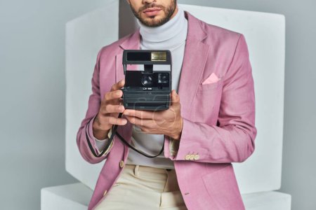 vista recortada del hombre moderno en blazer lila tomar fotos en la cámara vintage cerca de cubos blancos en gris