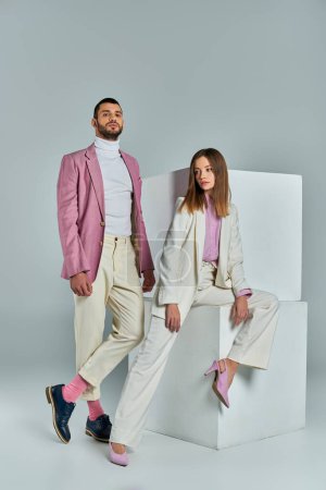 modern couple in pastel business attire posing near white cubes on grey, young professionals