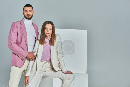 Téléchargez les photos : Femme en costume blanc et homme en blazer lilas regardant la caméra près de cubes blancs sur gris, usure tendance - en image libre de droit