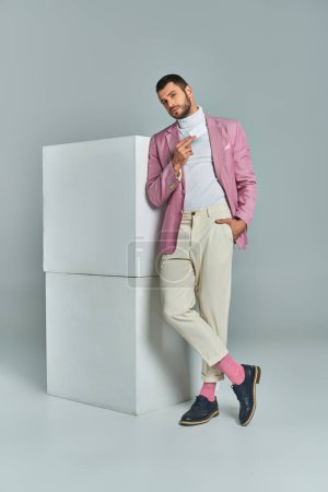 Foto de Hombre con estilo en blazer lila de pie con la mano en el bolsillo y la tarjeta de visita en blanco cerca de cubos en gris - Imagen libre de derechos