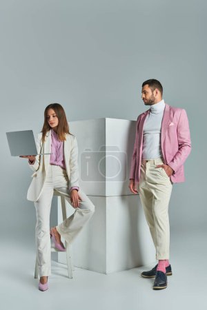 Photo for Woman in white suit with laptop near man in lilac blazer with hand in pocket next to cubes on grey - Royalty Free Image