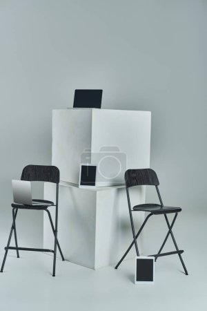 Foto de Portátiles y tabletas digitales con pantalla en blanco cerca de cubos blancos y sillas de oficina sobre fondo gris - Imagen libre de derechos
