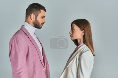 Téléchargez les photos : Vue latérale de jeune couple dans des blazers élégants se regardant sur gris, de façon minimaliste - en image libre de droit