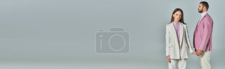 Téléchargez les photos : Femme élégante en costume blanc tenant la main avec l'homme en blazer lilas tout en se tenant sur gris, bannière - en image libre de droit