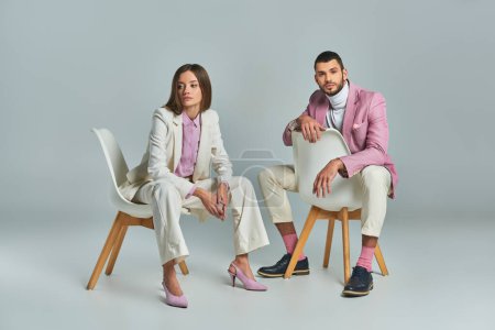 Téléchargez les photos : Mode couple d'affaires en pastel vêtements formels assis dans des fauteuils sur gris, mode minimaliste - en image libre de droit