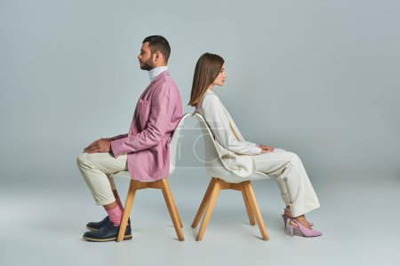 Téléchargez les photos : Couple moderne en tenue de travail assis dos à dos dans des fauteuils sur gris, minimaliste c mode - en image libre de droit