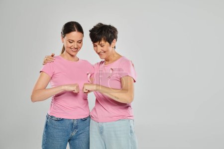 concepto de cáncer de mama, mujeres felices con cintas rosadas puño chocando contra fondo gris, libre de cáncer