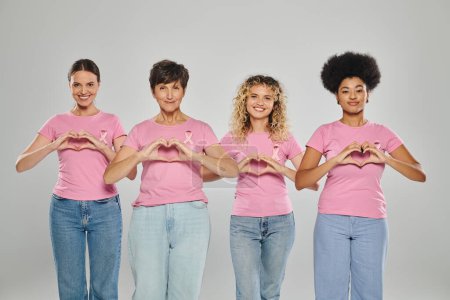 Brustkrebs-Bewusstsein, glückliche interrassische Frauen mit rosafarbenen Bändern, die Herz auf Grau zeigen, Vielfalt