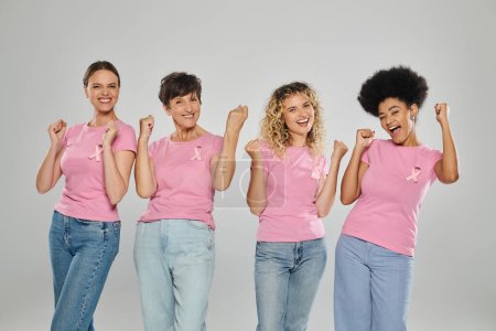 Téléchargez les photos : Sensibilisation au cancer du sein, excitées femmes interracial avec des rubans roses sur gris, diversité, sans cancer - en image libre de droit