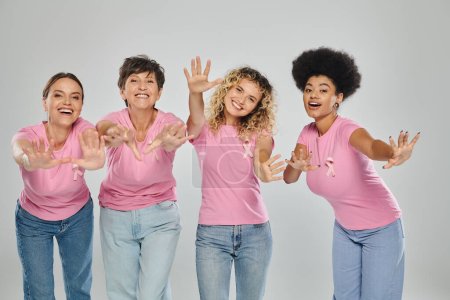 breast cancer awareness, joyful interracial women with pink ribbons on grey, diversity, cancer free