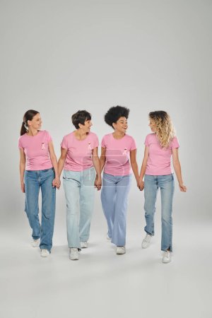 Brustkrebs-Bewusstsein, positive multikulturelle Frauen mit rosafarbenen Bändern, die gemeinsam auf grau laufen
