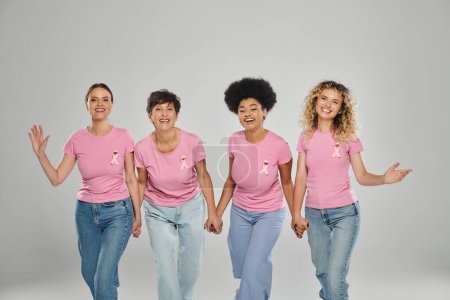 Brustkrebs-Bewusstsein, fröhliche multikulturelle Frauen mit rosafarbenen Bändern, die gemeinsam auf grau laufen