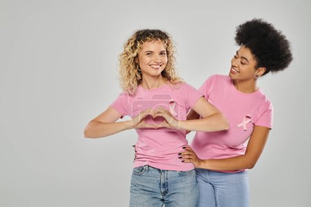 Brustkrebs-Bewusstsein, fröhliche gemischtrassige Frauen mit rosafarbenen Bändern vor grauem Hintergrund, Vielfalt