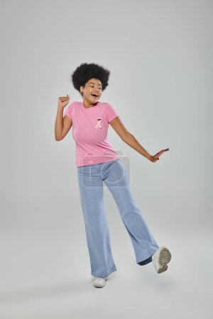 breast cancer awareness, excited african american woman with pink ribbon on grey, support campaign