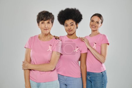 Foto de Concienciación sobre el cáncer de mama, felices mujeres multiculturales sonriendo sobre un telón de fondo gris, diferentes generaciones - Imagen libre de derechos