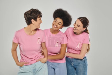 Téléchargez les photos : Sensibilisation au cancer du sein, femmes interracial souriantes, posant sur fond gris, différentes générations - en image libre de droit
