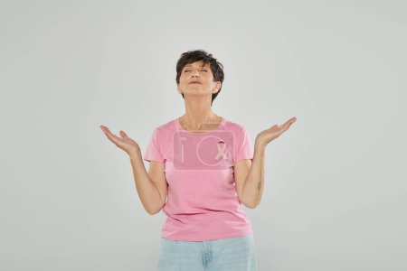 breast cancer awareness, happy mature woman with pink ribbon, grey backdrop, joy, meditation