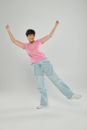 breast cancer awareness, happy mature woman with pink ribbon, grey backdrop, emotional gesturing