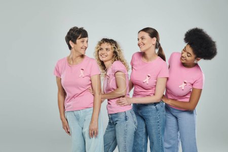multicultural women different age smiling on grey backdrop, support, breast cancer awareness