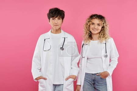 happy female doctors in white coats standing on pink backdrop, smile, breast cancer awareness, women