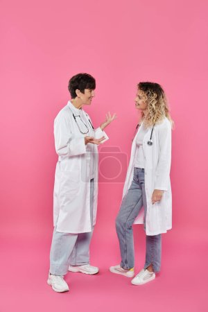 heureuses femmes médecins en manteaux blancs bavardant sur fond rose, sensibilisation au cancer du sein, femmes